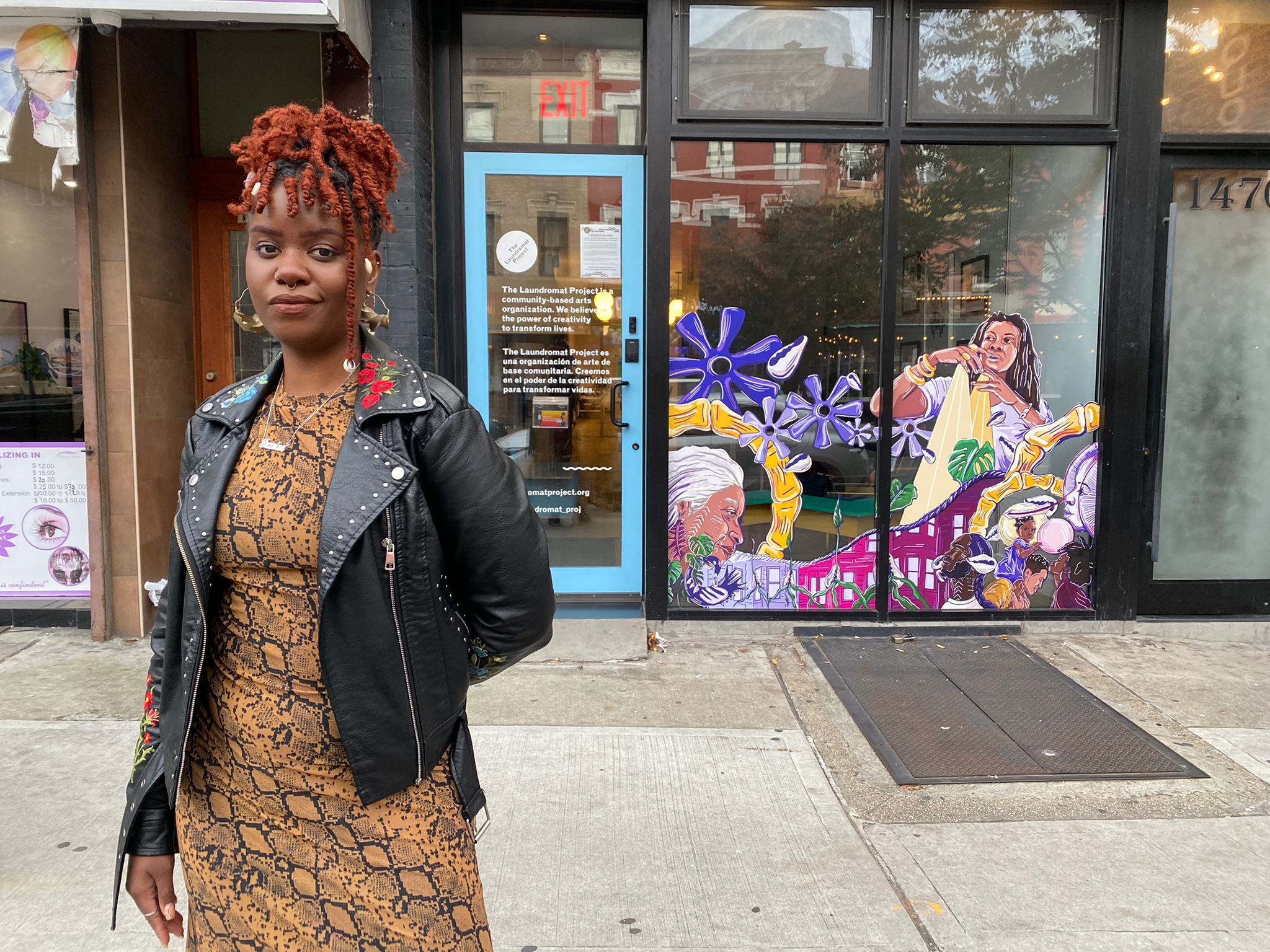 Artist Jazmine Hayes stands, confident, in front of The Laundromat Project storefront on Fulton Street. Her artwork is in the background.