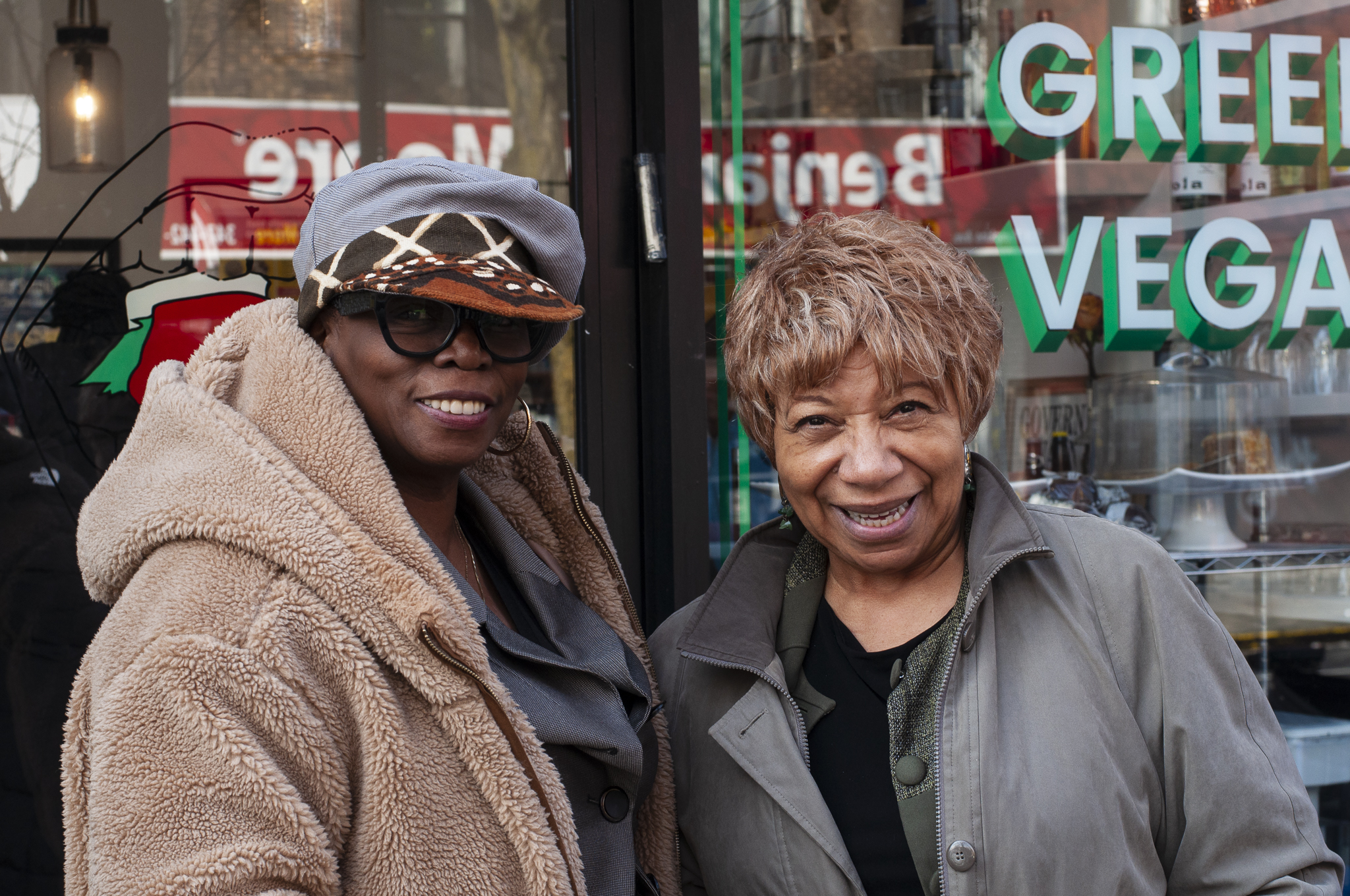 Photograph of two members of the United Order of the Tents bundled up against the cold, standing in front of Greedi Vegan restaurant.
