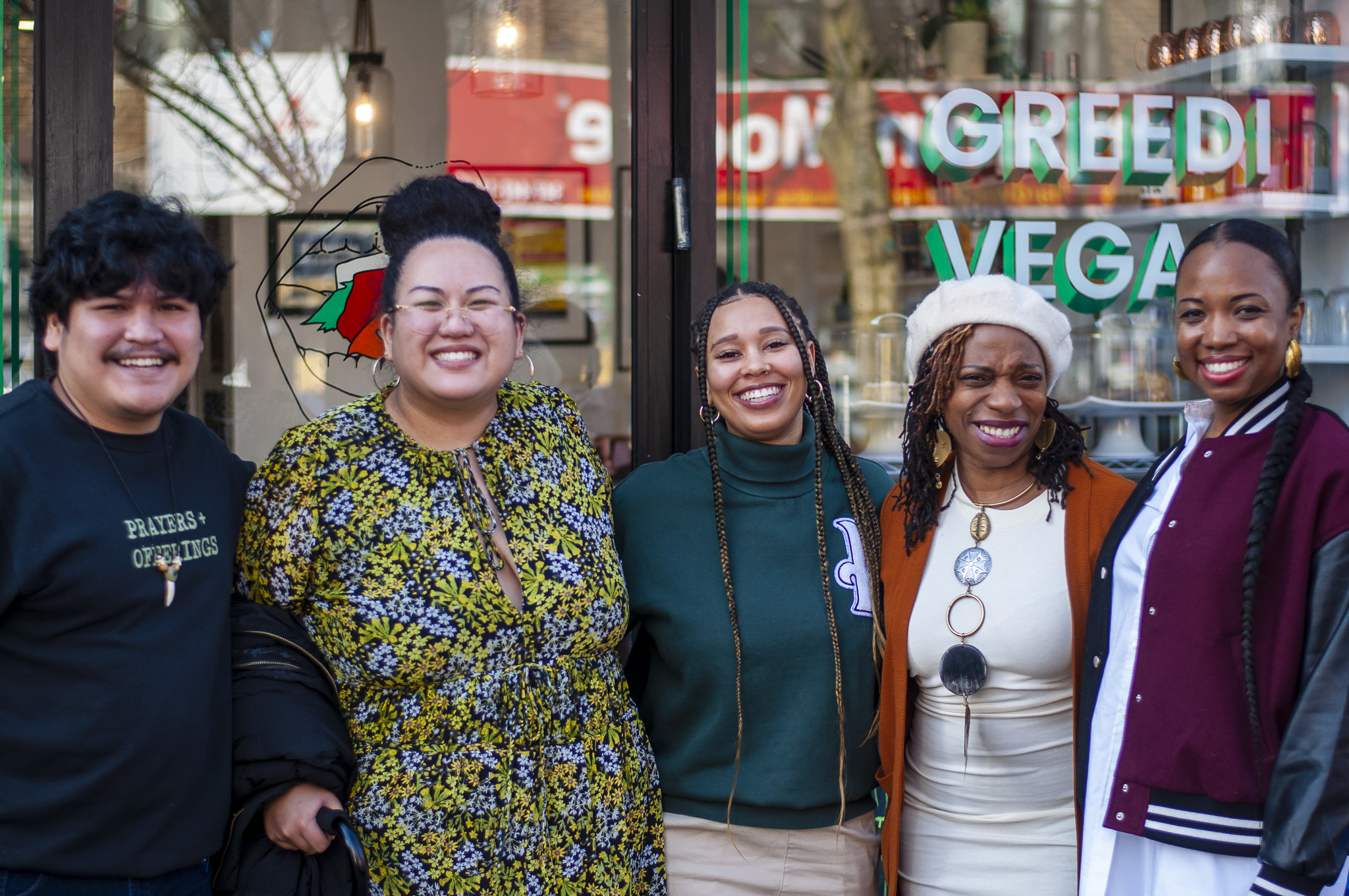 Four LP staff members from the Community Engagement team smile alongside The LP's Executive Director, Ayesha Williams, in front of Greedi Vegan Restaurant